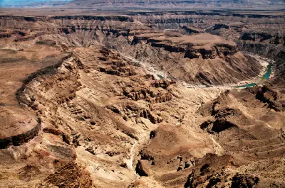 Wide elevated view across the layered cliffs and winding river of Fish River Canyon in southern Namibia under dry desert light.