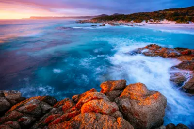 Orange-lichen-covered granite rocks and turquoise waves at sunrise at Friendly Beaches in Freycinet National Park, Tasmania.