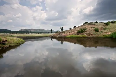 Farm dam reflecting large thunderclouds with grassy hills and ridges in the Vredefort Dome World Heritage Site, South Africa.