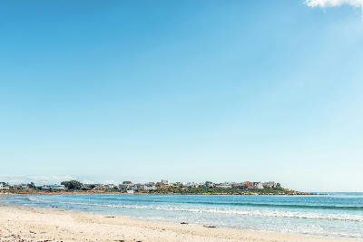 Sandy beach and calm bay waters with coastal houses along the shoreline of Britannia Bay, Western Cape, South Africa.