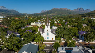 Drone view of Stellenbosch Town Centre featuring the historic white Dutch Reformed Church, tree-lined streets, and Cape Winelands mountains in South Africa.