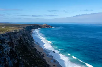 Rugged limestone cliffs above a narrow sandy beach with turquoise waves near Remarkable Rocks, Kangaroo Island, South Australia.