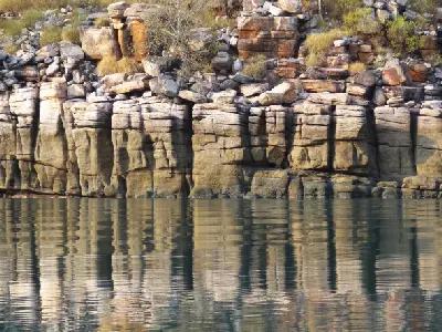 Weathered sandstone formations reflected in the calm water along the banks of the Prince Regent River.