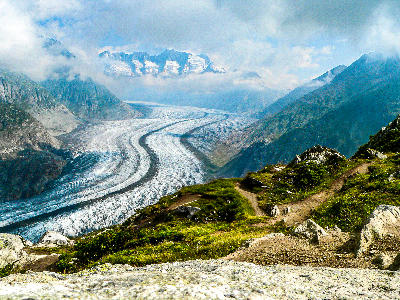 Aletsch Glacier winding through a high alpine valley beneath cloud-covered peaks, viewed from a mountain trail in Switzerland.