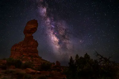 Balanced Rock silhouette under a clear night sky with Milky Way and dense stars in Arches National Park Utah