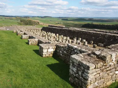 Remains of the Roman granary at Housesteads Fort in Northumberland, showing rows of stone floor supports, ancient walls and rolling countryside.