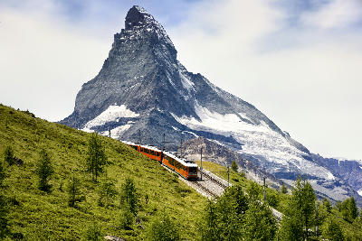 Gornergrat railway train ascending alpine slopes with the Matterhorn rising in the background near Zermatt, Switzerland.