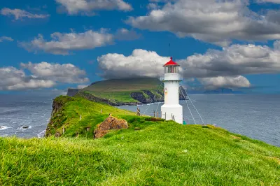 White lighthouse with red roof on a cliff ridge at Mykines Hólmur overlooking the Atlantic Ocean, Faroe Islands.