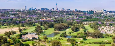 Aerial view of Johannesburg with jacaranda trees, green urban parklands and the city skyline rising above Gauteng, South Africa.