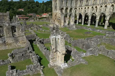 Elevated aerial view of Rievaulx Abbey showing the excavated monastery foundations, ruined stone buildings and towering Gothic church arches in North Yorkshire, England.