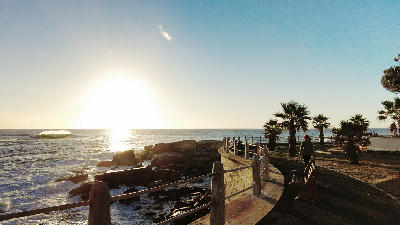 Woman walking along the Sea Point Promenade boardwalk at sunset beside the Atlantic Ocean in Cape Town, South Africa.