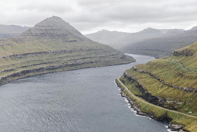 Steep basalt mountain walls and winding coastal road along Funningsfjørður fjord on Eysturoy, Faroe Islands.
