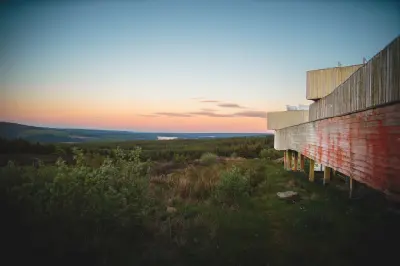 Timber exterior of Kielder Observatory overlooking dense conifer forest and distant Kielder Water beneath a pink and blue twilight sky.