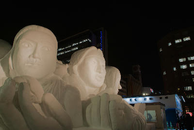Illuminated snow sculpture of human figures at night during the Sapporo Snow Festival in Odori Park, Sapporo, Japan.
