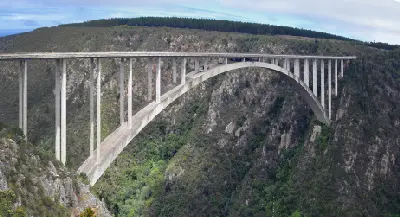 Side view of Bloukrans Bridge crossing the deep Bloukrans River Gorge in the Tsitsikamma region of South Africa, showing the bridge arch, forested canyon walls and bungy jumping platform beneath the deck.