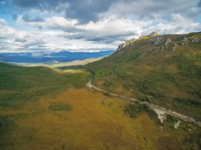 Aerial view of Gordon River Road winding beneath rugged mountains in western Tasmania, Australia.