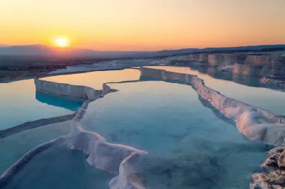 Sunset over the white travertine terraces and shallow thermal pools of Pamukkale, Turkey, with mountains on the horizon.