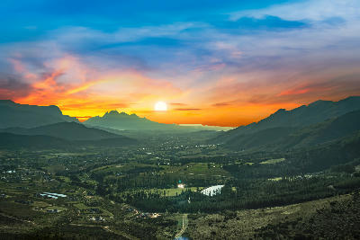 Golden sunset over Franschhoek Valley viewed from Franschhoek Pass with layered mountain ranges and Cape Winelands scenery in South Africa.