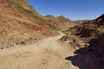 A rugged gravel track winds through a rocky mountain valley in Richtersveld National Park, surrounded by colourful desert slopes and barren wilderness landscapes.