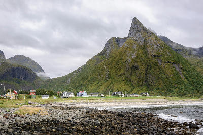 Rocky and sandy shoreline at Ersfjord with village houses at the base of a sharply rising green mountain ridge