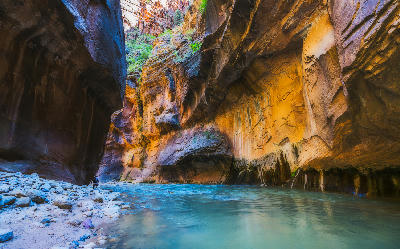 Hiker wading through the Virgin River inside the narrow sandstone walls of The Narrows in Zion National Park, Utah.