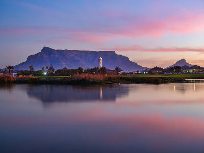 Milnerton Lagoon and lighthouse with reflections of Table Mountain at sunset in Cape Town, South Africa.