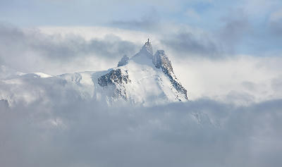 Aiguille du Midi peak emerging through clouds in the Mont Blanc Massif with snow-covered slopes.