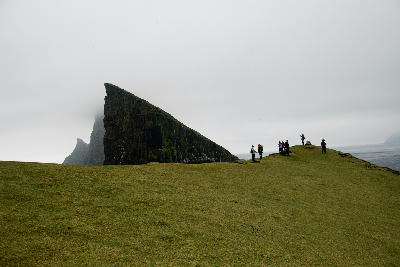 Hikers standing on a grassy cliff near the Drangarnir sea stacks on Vágar Island, Faroe Islands.