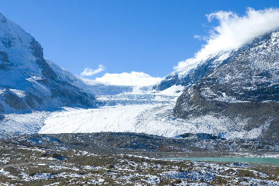 Athabasca Glacier flowing from the Columbia Icefield in Jasper National Park, surrounded by snow-covered mountains and rocky foreground terrain