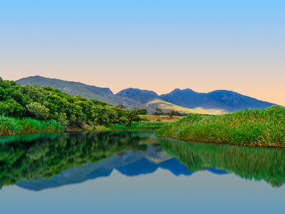 Calm reflection of the Klein River and Kleinrivier Mountains near Stanford, with reeds and green riverbanks in the Western Cape, South Africa.