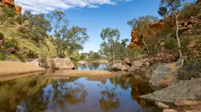 Waterhole and eucalyptus trees framed by red-orange rock walls at Simpsons Gap, or or Rungutjirpa, in the West MacDonnell Ranges.