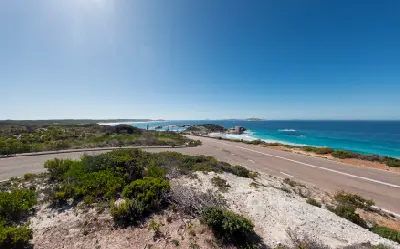 Great Ocean Drive winding through coastal heath beside granite shoreline and turquoise ocean near Esperance, Western Australia.