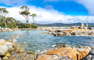 Granite boulders covered with orange lichen beside clear water in the Bay of Fires Conservation Area, northeast Tasmania.