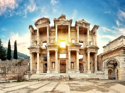 Ornate two-story façade of the ancient Library of Celsus at Ephesus, framed by stone ruins beneath a bright blue sky.