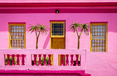 Close-up of a bright pink house with wooden windows and balcony railings in Bo-Kaap, Cape Town, South Africa.