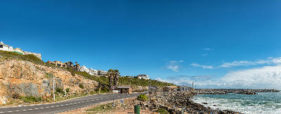 Coastal road and rocky shoreline at Yzerfontein Harbour, with ocean waves, harbour breakwaters and homes overlooking the Atlantic coast.