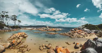Sandy cove with clear water and orange lichen-covered granite rocks at Binalong Bay, Tasmania.