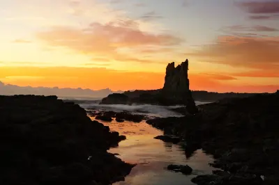 Cathedral Rocks silhouetted against a vivid orange sunrise, with waves and tidal pools reflecting the sky along the rocky Kiama coastline.