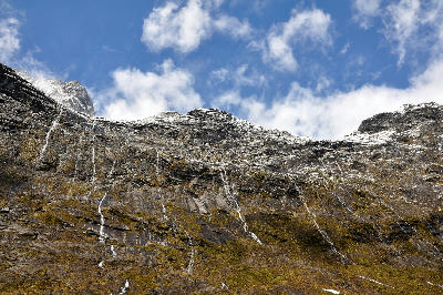 Cliffs and thin waterfalls on the steep valley walls of Cleddau Valley near the Homer Tunnel in Fiordland National Park, New Zealand.