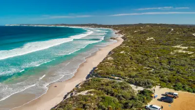 Aerial view of Pennington Bay on Kangaroo Island, South Australia, showing turquoise ocean waves, a long sandy beach, coastal dunes and surrounding native vegetation.