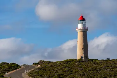 Cape du Couedic Lighthouse with its red lantern roof and limestone tower beside a winding road on Kangaroo Island, South Australia.