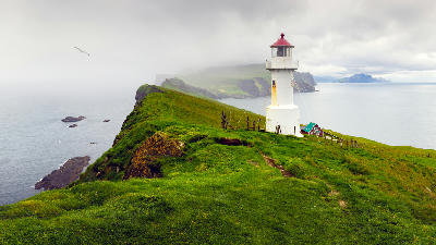 White lighthouse with red roof on a narrow ridge at Mykines Hólmur above the Atlantic Ocean, Faroe Islands.