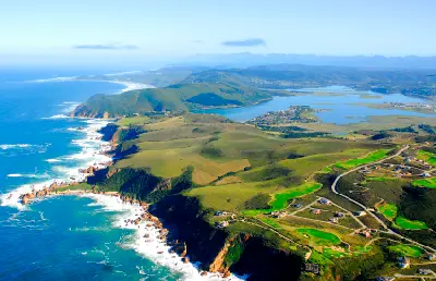 Aerial view of the Knysna coastline, lagoon and estuary system on South Africa’s Garden Route, showing forested hills, rocky cliffs and the Indian Ocean.