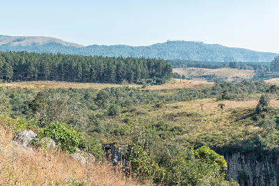 Visitors standing at the Mac Mac Falls viewpoint overlooking a forested canyon, pine plantations and rolling hills on the Panorama Route in Mpumalanga, South Africa.