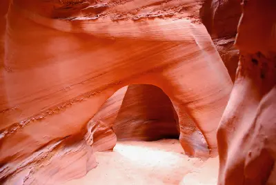 Smooth red sandstone walls form a natural arch above the narrow sandy passage through Peek-a-Boo Gulch slot canyon.
