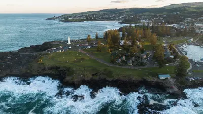 Aerial view across Kiama Harbour and lighthouse with waves breaking along the rocky coastline and beaches extending south along the Illawarra Coast.