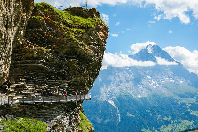 First Cliff Walk hugging a steep rock face with visitors on a narrow walkway overlooking alpine valleys and peaks near Grindelwald, Switzerland.