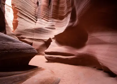 Narrow passage inside Canyon X near Page Arizona with smooth curved sandstone walls and sandy floor in a quiet slot canyon.