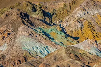 Vivid mineral-stained slopes at Artist’s Palette in the Black Mountains, Death Valley National Park, California, revealing oxidized deposits in green, white, and ochre tones across eroded ridgelines.