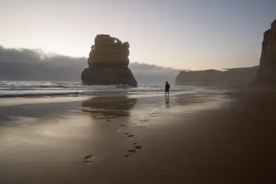 Person walking across wet sand toward a towering limestone sea stack at Gibson Steps Beach, Victoria.